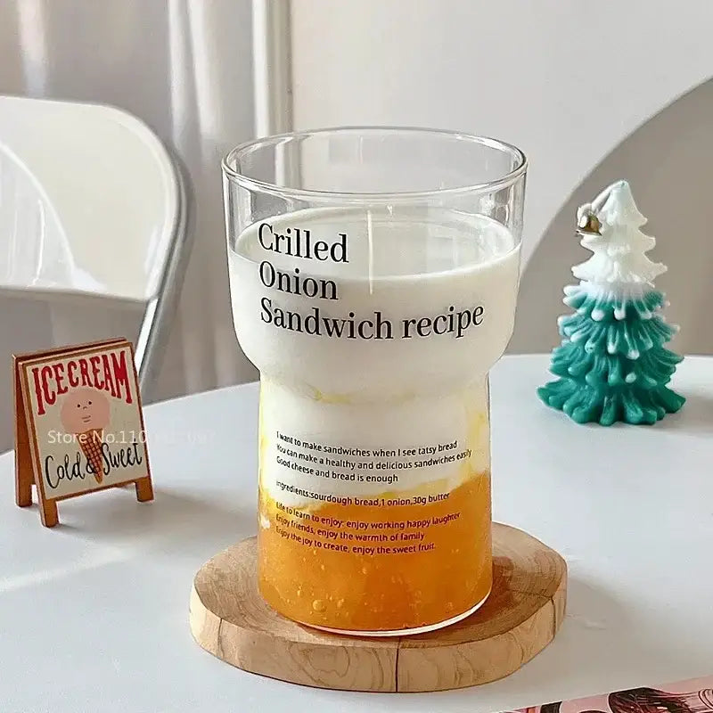 Clear glass coffee mug with black printed grilled onion sandwich recipe text filled with layered orange and white liquid
