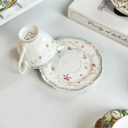 A delicate white porcelain teacup and saucer set with a brilliant flowers pattern in soft pink green and brown hues