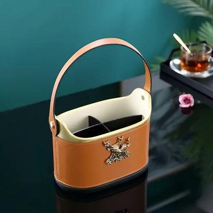 Brown leather desktop storage basket with gold deer emblem, tan leather tea caddy interior, and curved handle for easy carrying