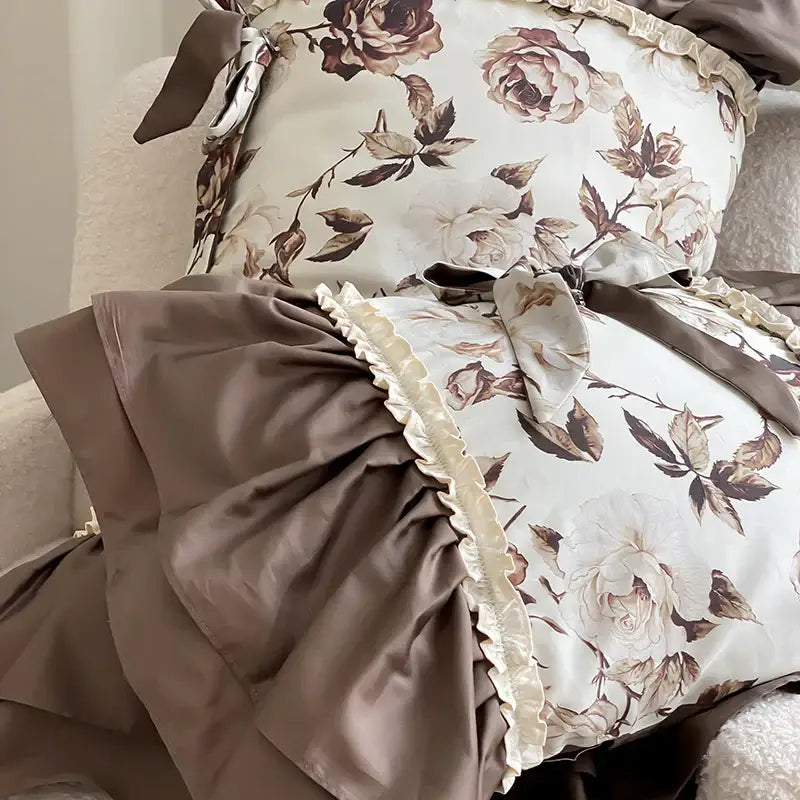 A cream-colored pillow with brown vintage flowers pattern, ruffled edges, and satin bows in a decorbites bedding set
