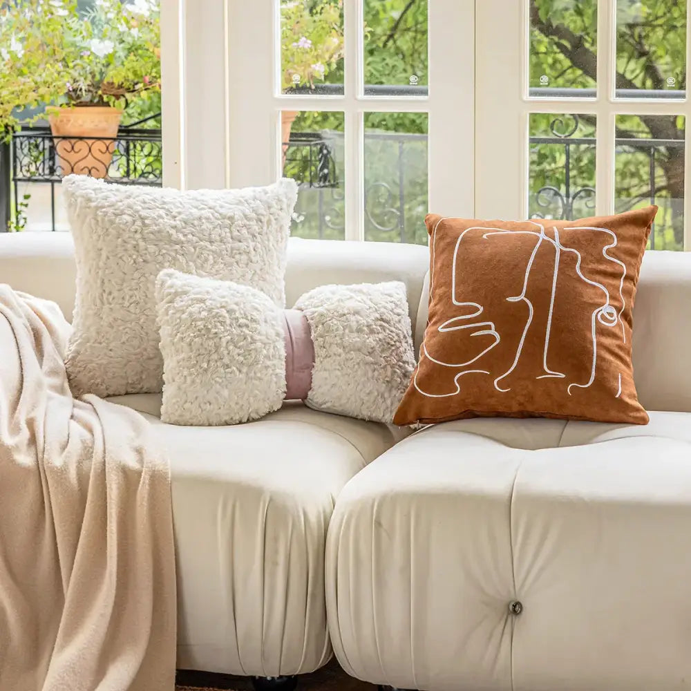 A warm brown velvet cushion cover with white decorbites geometric embroidery on a cream sofa for living room decor