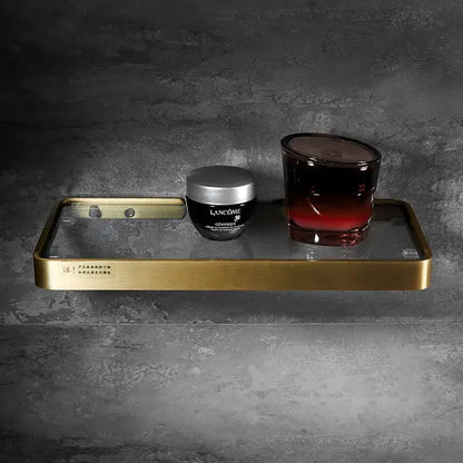Brushed gold and black corner shelf with glass tier holding lancôme skincare and dark red gradient candle decorbites brushed gold bathroom