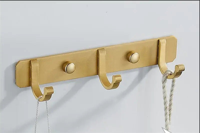 Brushed gold metal wall-mounted robe hooks with three curved hooks and decorative round knobs by decorbites