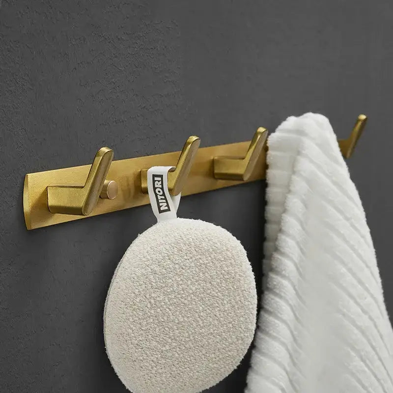 Gold-colored brushed gold robe hooks with three metal hooks holding a white loofah and towel by decorbites