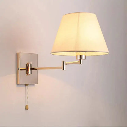 A sleek brushed brass wall lamp with a cream fabric shade and adjustable rocker arm for bedroom use