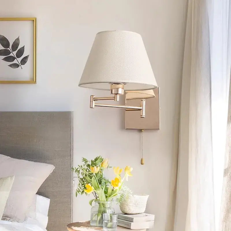 A sleek gold-finished wall lamp with tapered cream shade and adjustable rocker arm for bedroom lighting