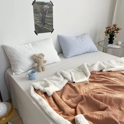 Soft peach-colored fleece blanket with plush white border draped over bed from decorbites camellia jacquard lamb collection