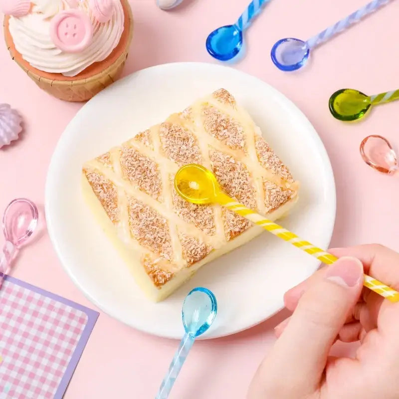 A yellow and white striped plastic spoon with a glossy finish resting on a coconut cake from decorbites colorful glass stirring set