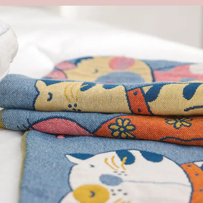 Stacked fabric pieces of decorbites cartoon boho bedspread featuring pastel cartoon cat designs on woven cotton material