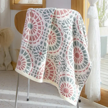 A soft white cotton gauze bath towel with pink and gray floral motifs draped over a wooden chair back decorbites cotton gauze bath towel