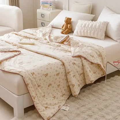 Cream-colored quilted cooling summer blanket with small brown teddy bear pattern and stitched edges for bedroom use