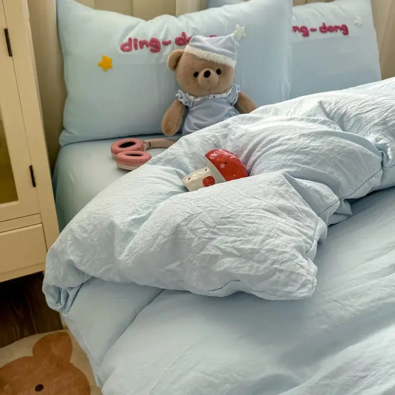A plush teddy bear in a light blue nightgown and star hat sits on a decorbites cartoon towel embroidery light blue bedding set