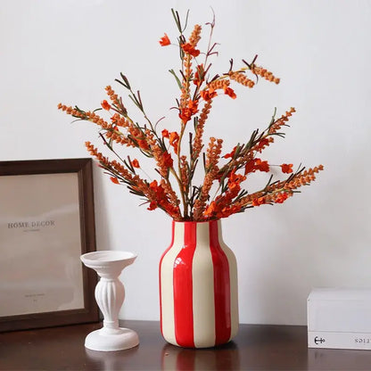Glossy red and cream vertically striped ceramic vase holding orange artificial flowers in a red striped design