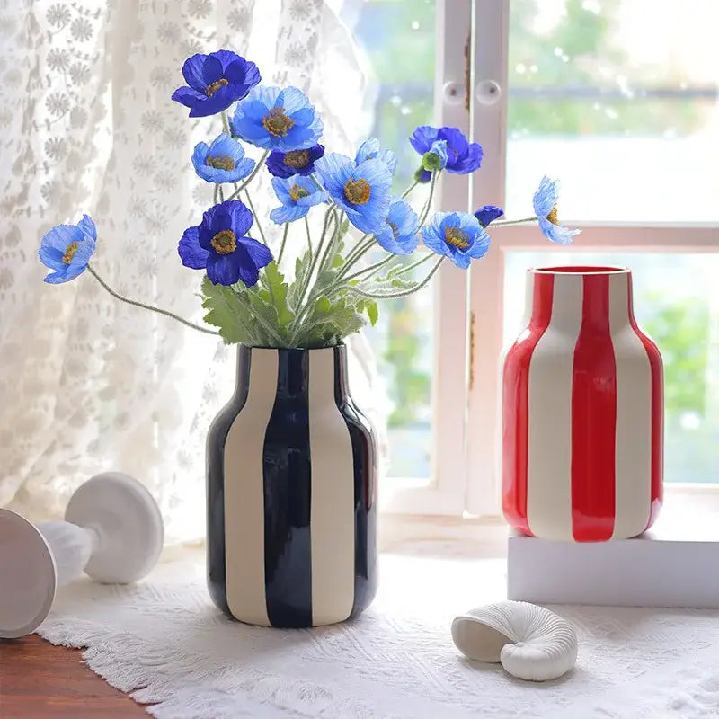 A sleek black and cream striped ceramic vase holding vibrant blue poppies, ideal as a decorative ceramic vase