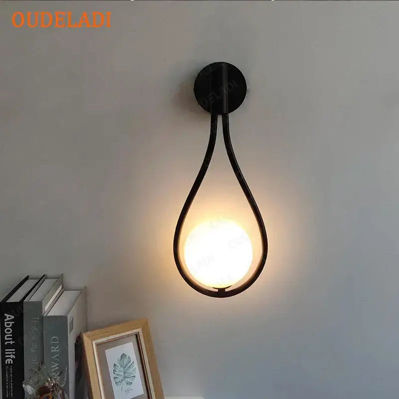 Black metal wall sconce with teardrop frame and warm glowing bulb featuring decorbites black glass ball decor