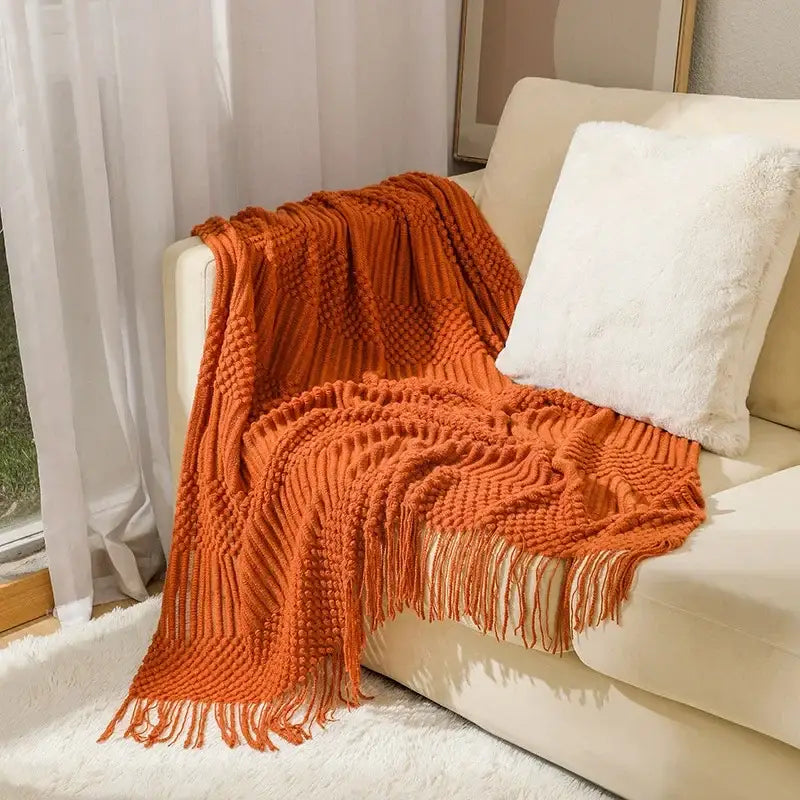 A cozy knitted sofa blanket in burnt orange with a chunky ribbed pattern and fringe for living room comfort