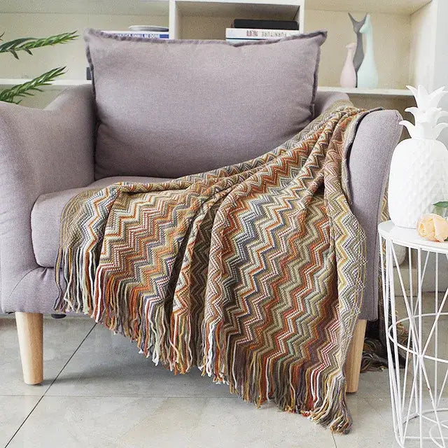 A cozy multicolored zigzag knit throw blanket with fringed edges draped over a gray armchair by decorbites houndstooth throw