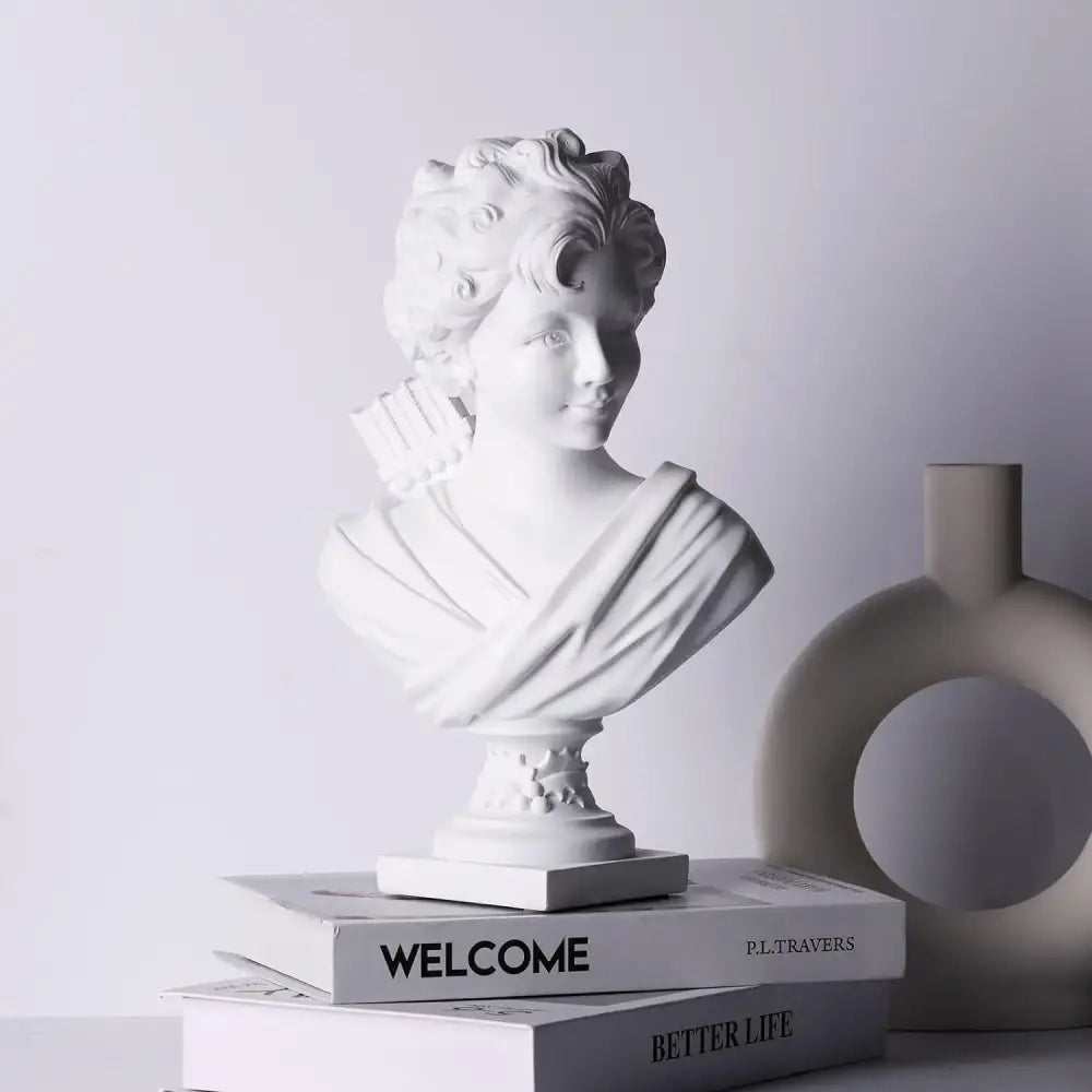 Classical white cupid statue plaster sculpture with curly hair and draped fabric resting on stack of books for decor