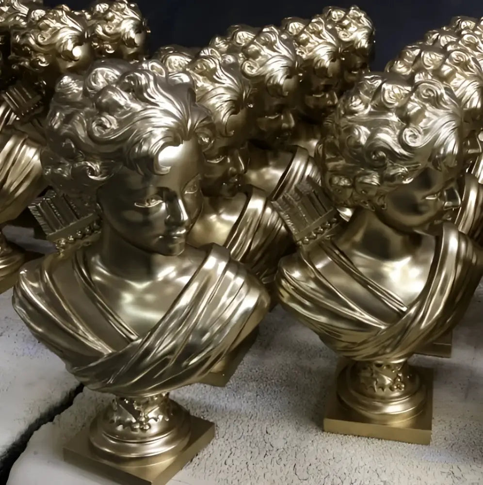 Golden metallic cupid statue plaster sculpture with intricate curly hair and draped fabric on ornate square bases