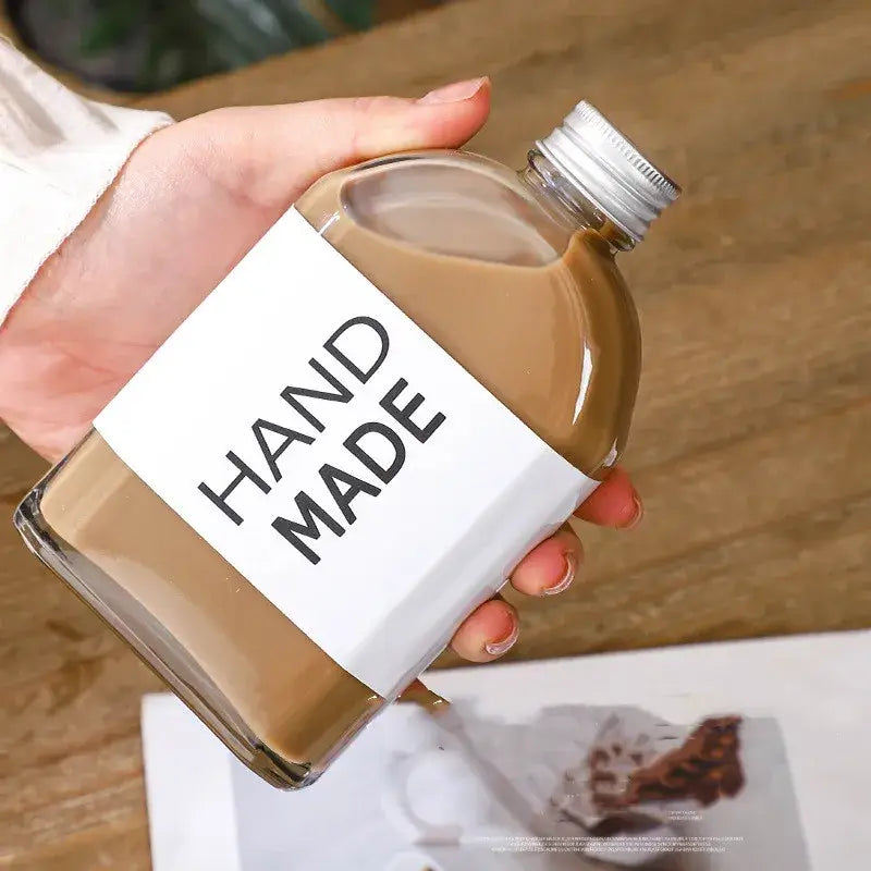 Clear glass beverage bottles with silver caps featuring a handmade label filled with brown liquid for kitchen juicing set