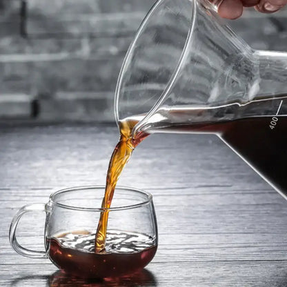 Clear glass coffee pot with stainless steel filter pouring dark coffee into a matching clear glass mug