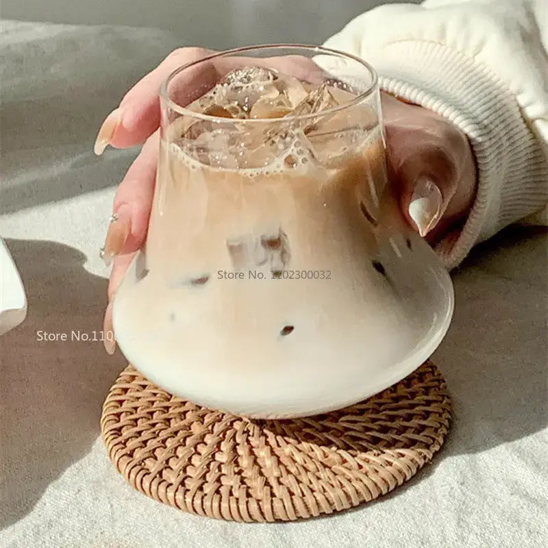 Clear glass cold brew latte drinkware set with wooden coaster featuring a tumbler filled with iced coffee on a rattan coaster