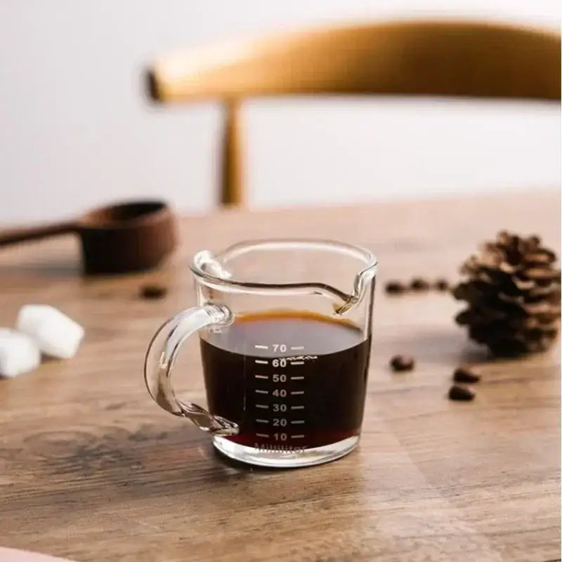 Clear glass espresso measuring cup with handle and spout marked in milliliters from 10 to 70 for precise measuring