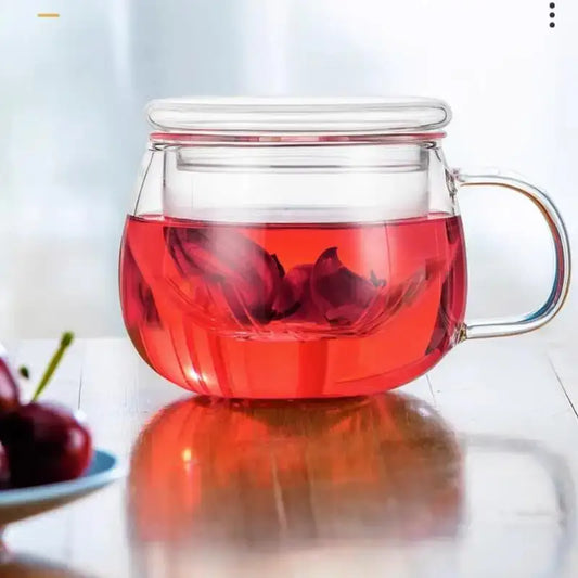 Clear glass floral tea pot with matching lid and handle filled with vibrant red hibiscus tea for floral tea cup use