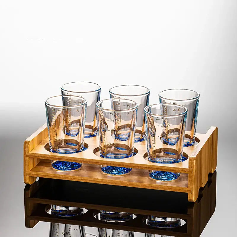 Set of six decorbites clear glass liquor cups with blue-tinted bases and measurement markings in a wooden rack