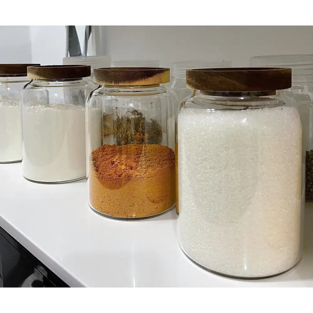 Clear kitchen glass jars with acacia lids in dark wood, containing various dry ingredients for food storage