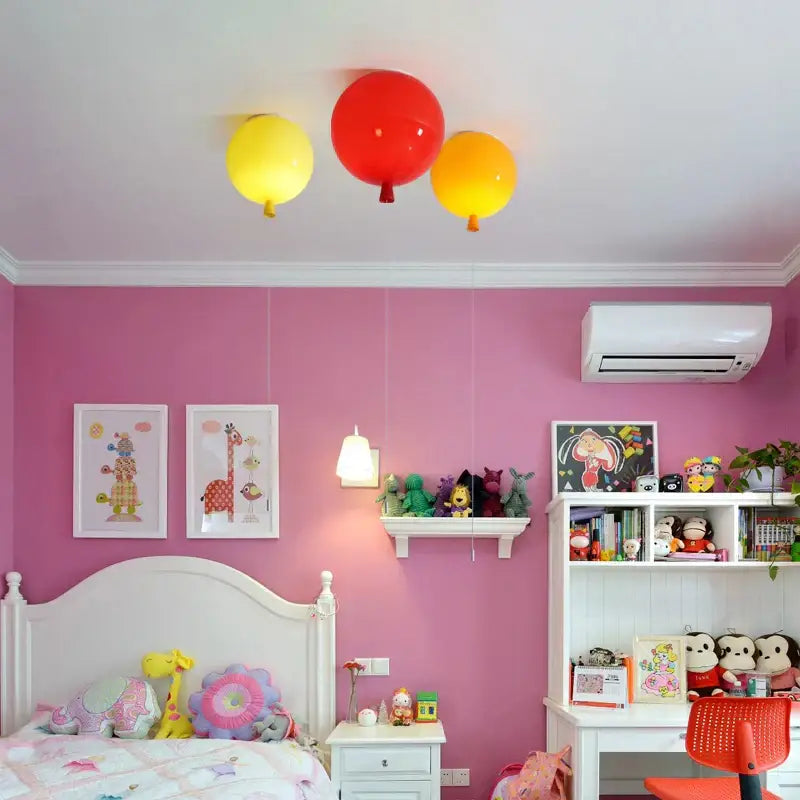 Three colorful balloon ceiling sconce lamps in red yellow and orange hang above a pink bedroom for decor