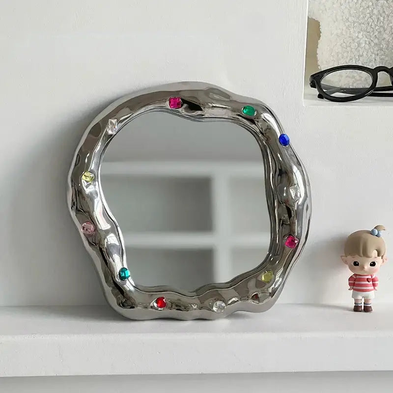 A shiny irregular edge silver ceramic makeup mirror adorned with colorful gemstones for bedroom use