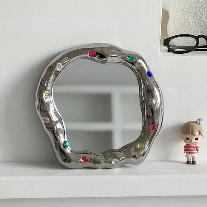 A shiny irregular edge silver ceramic makeup mirror adorned with colorful gemstones for bedroom use