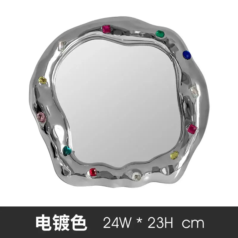 A sleek silver-plated ceramic makeup mirror with an irregular edge adorned with colorful gemstones for bedroom use