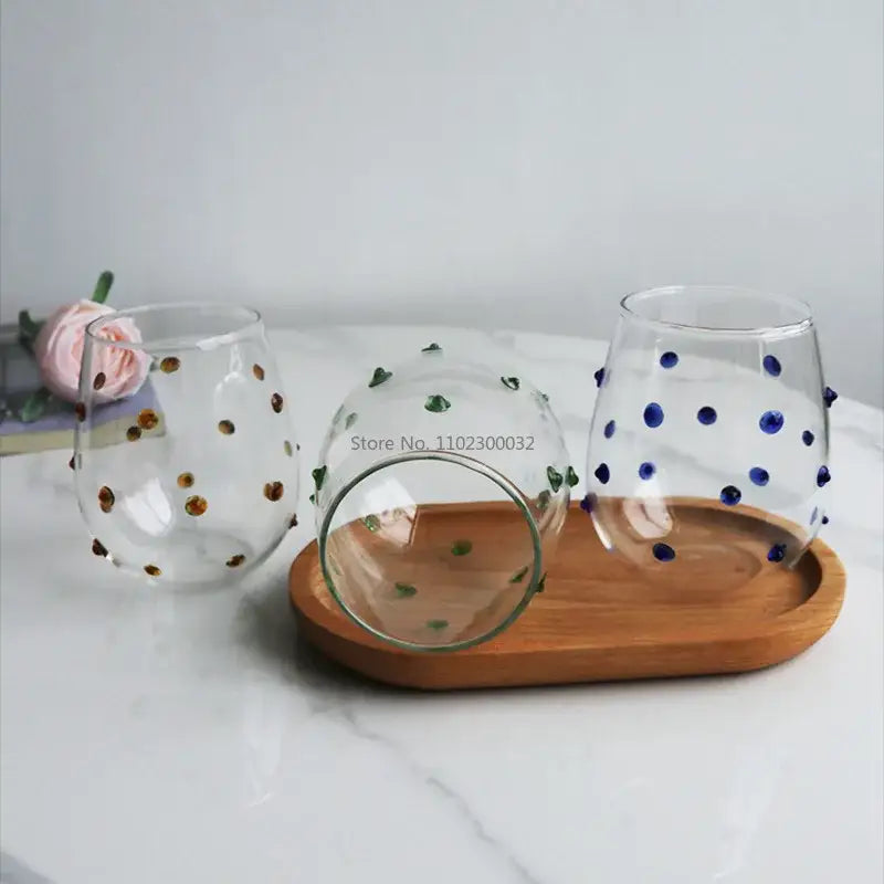 Three clear stemless wine glasses with colorful gold blue and green wave dots arranged on a wooden tray