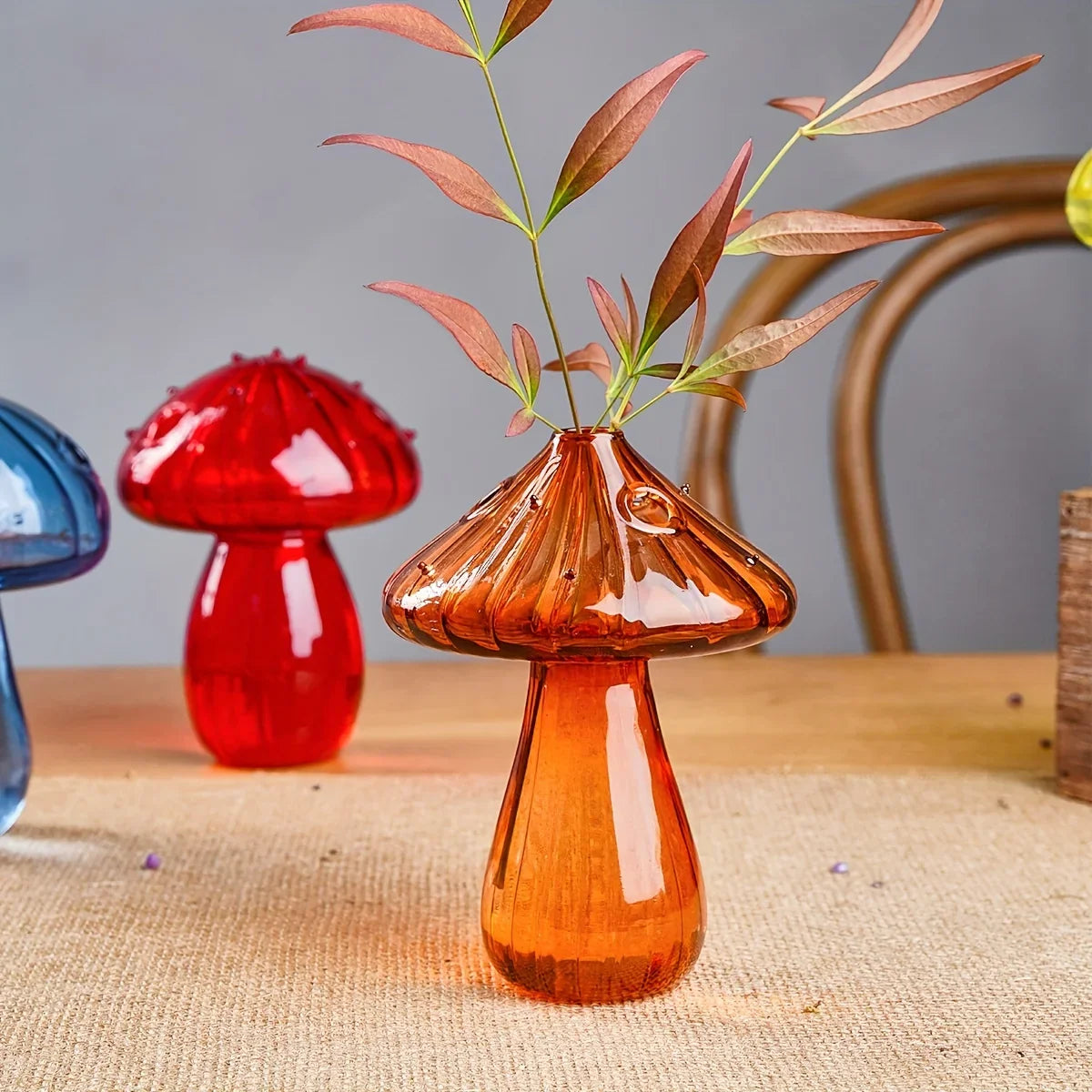 A translucent amber glass mushroom vase with ribbed cap holding delicate reddish-green foliage for home decor