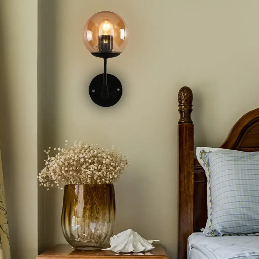 Contemporary wall light featuring warm amber globe glass shade with black metal base for bedroom use