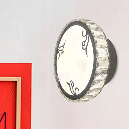 Contemporary black circular wall light with clear crystal trim and black ornamental swirls on a white panel