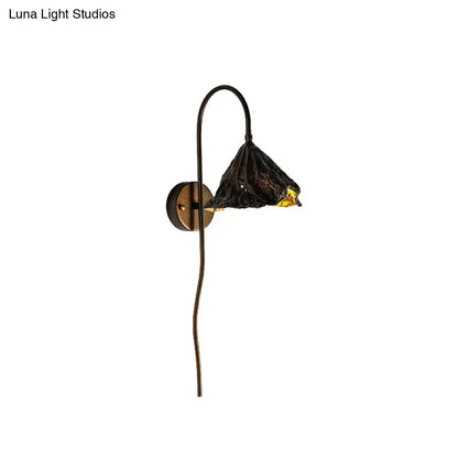 Contemporary black wrought iron wall light with textured lotus leaf glass shade and amber interior glow for living room