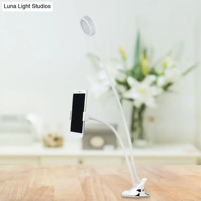 White flexible led desk lamp with clip-on base and adjustable arm holding smartphone for bedroom use