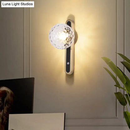 Contemporary clear glass wall lamp with faceted globe and metallic base showcasing fixture width for living room use
