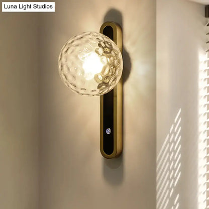 Gold finished contemporary wall lamp with textured clear glass globe and fixture width ideal for living room sconce