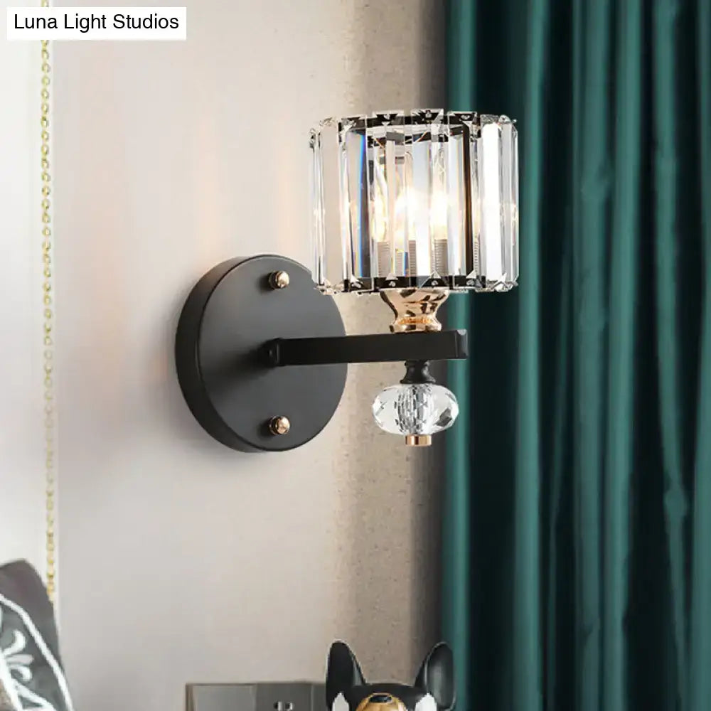 A contemporary clear ribbed glass drum sconce light with black metal base and cylindrical crystal shade for bedroom use