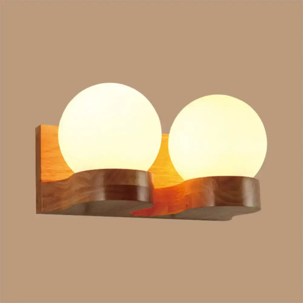 Contemporary warm-toned wood sconce light fixture with two cream glass globe shades for living room wall