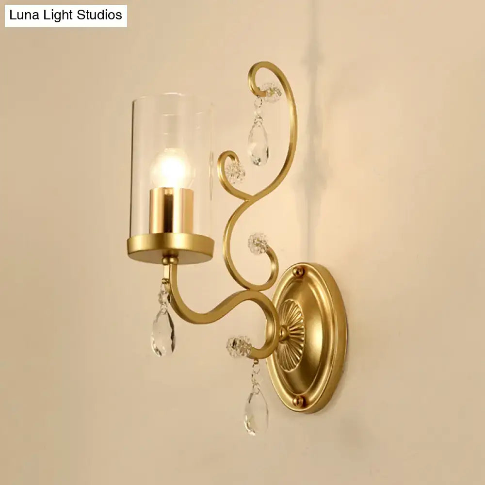 Contemporary gold wall light with clear glass cylindrical shade and crystal teardrop accents for bedroom use