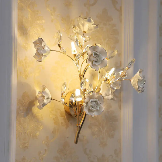 Elegant gold-toned wall lamp with white porcelain roses and crystal accents for contemporary bedroom light fixture