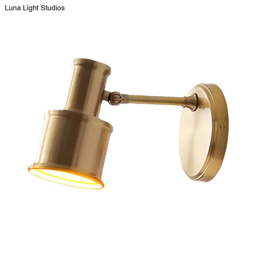 Brass-finished metal cylinder wall sconce with adjustable articulated arm and cylindrical shade for bedroom lighting