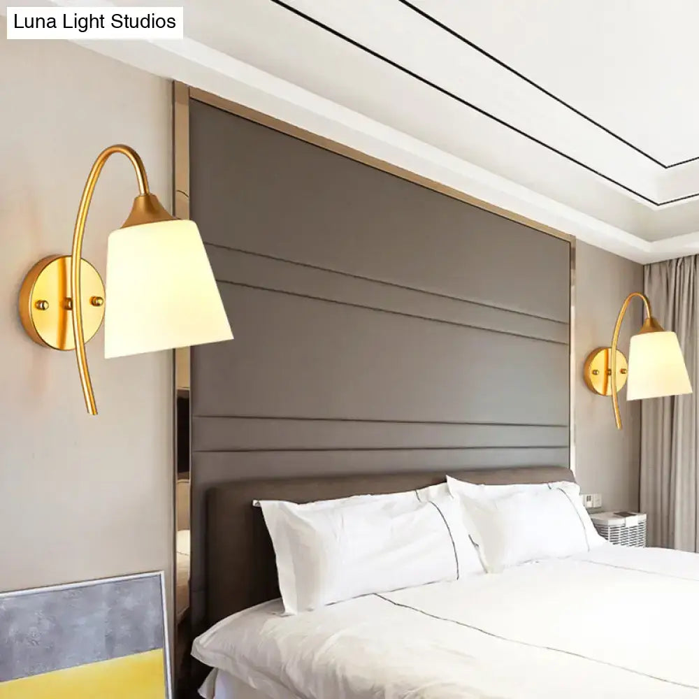 Contemporary gold milk glass wall lamp with a gold-toned curved arm and off-white lampshade for bedroom sconce use
