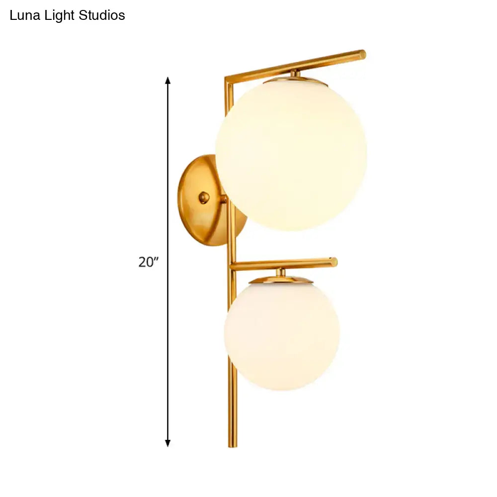 Contemporary gold-toned bedroom wall sconce light fixture with two frosted spherical glass shades and shade width detail