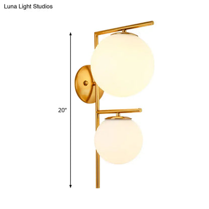 Contemporary gold-toned bedroom wall sconce light fixture with two frosted spherical glass shades and shade width detail